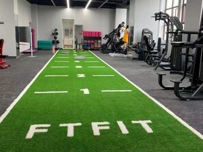 Une salle de sport dotée d’une piste d’athlétisme en gazon synthétique vert, avec des numéros et le mot « FTFIT » qui y sont inscrits.