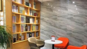 A modern library with a marble wall, a wooden bookshelf, and two orange chairs around a small table. - Greentree Inn Yingtan Xinjiang New District Munici (Yingtan)