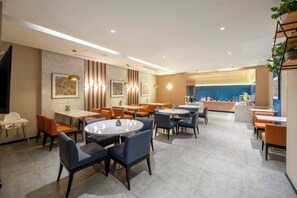 A modern hotel lobby with round tables and chairs, a reception desk, and a view of the kitchen area. - Jinjiang Inn (Wuxi New District National Software Park) (Wuxi)