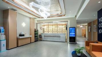 A hotel reception area with a reception desk, a digital screen, and seating.