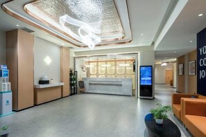 Ein Hotel-Empfangsbereich mit Empfangsschalter, digitalem Bildschirm und Sitzgelegenheiten.