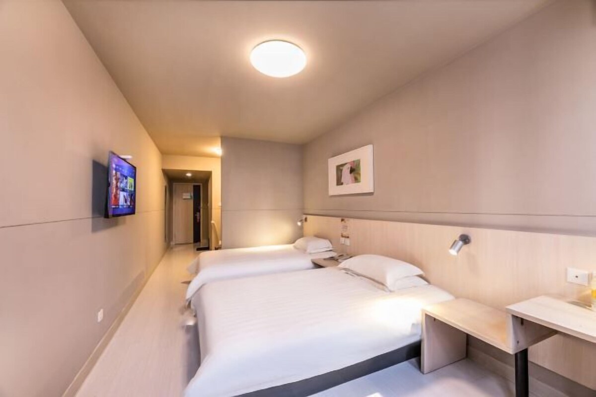 A hotel room with three beds, a bedside table, a TV, and a picture on the wall.
