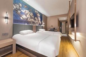 A hotel room with two beds, a large floral mural, a wooden floor, and a hallway with a mirror.