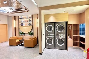 Habitación de hotel con sofá, una mesita de centro, lavadora y una estantería con libros.