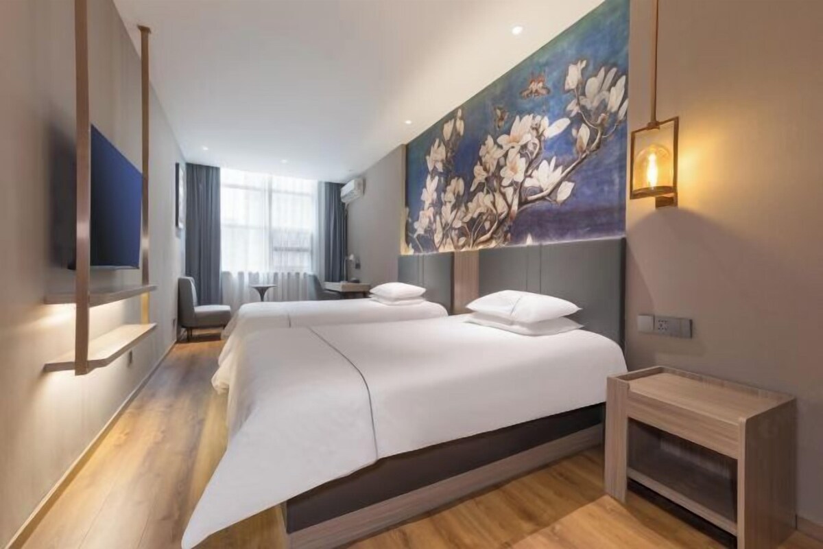 A modern hotel room with a large bed, a flat-screen TV, a painting on the wall, and a small bedside table.