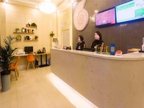 Zona de recepción con mostrador, dos empleados, una computadora y un gran elemento decorativo en la pared.