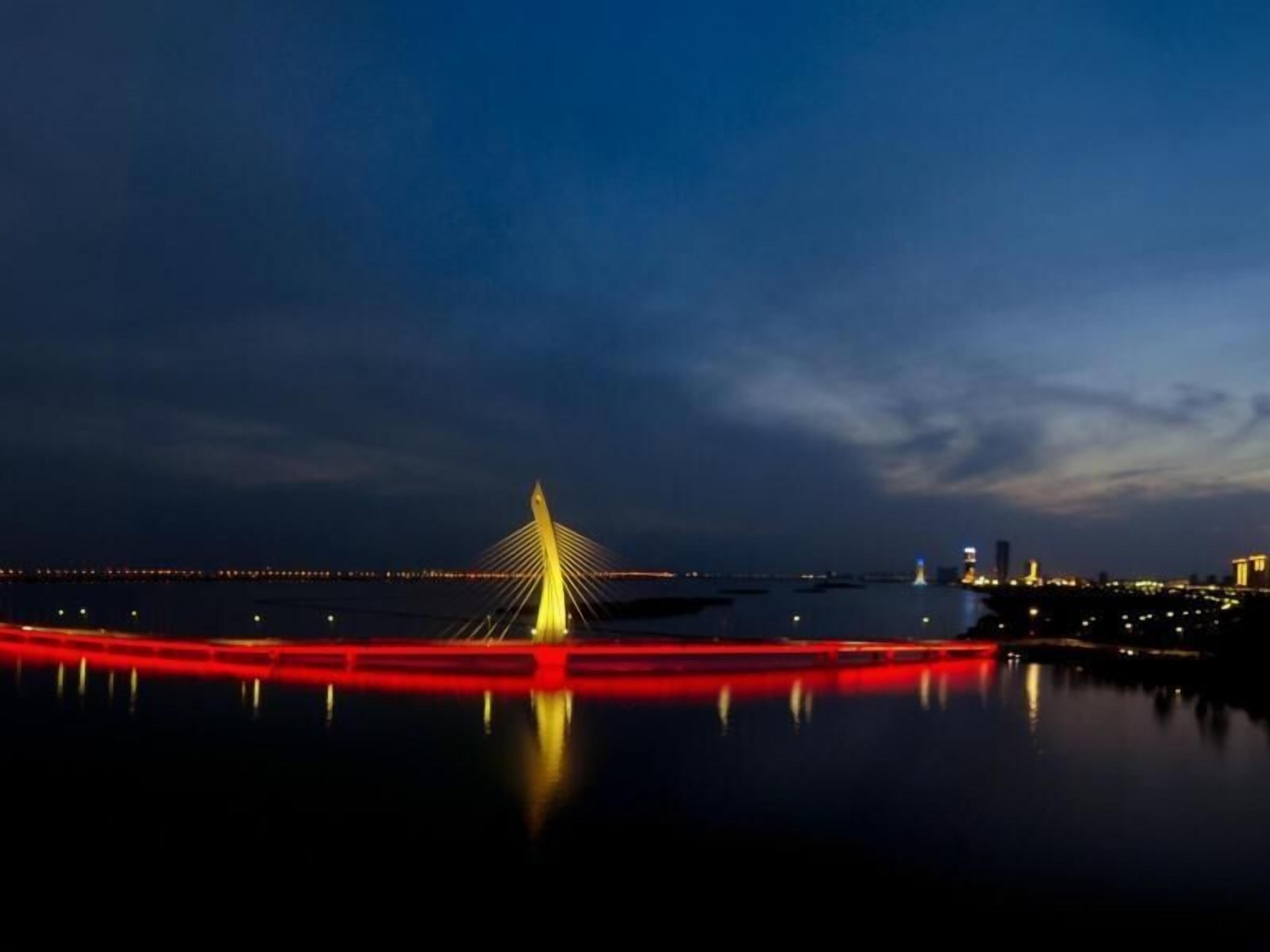 A nighttime view of a bridge with a distinctive cable design, reflecting on calm water.