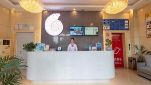 A hotel reception desk with a large illuminated sign, a receptionist, and a digital screen displaying information. - Shell Changzhou University City Science and Educat (Changzhou)