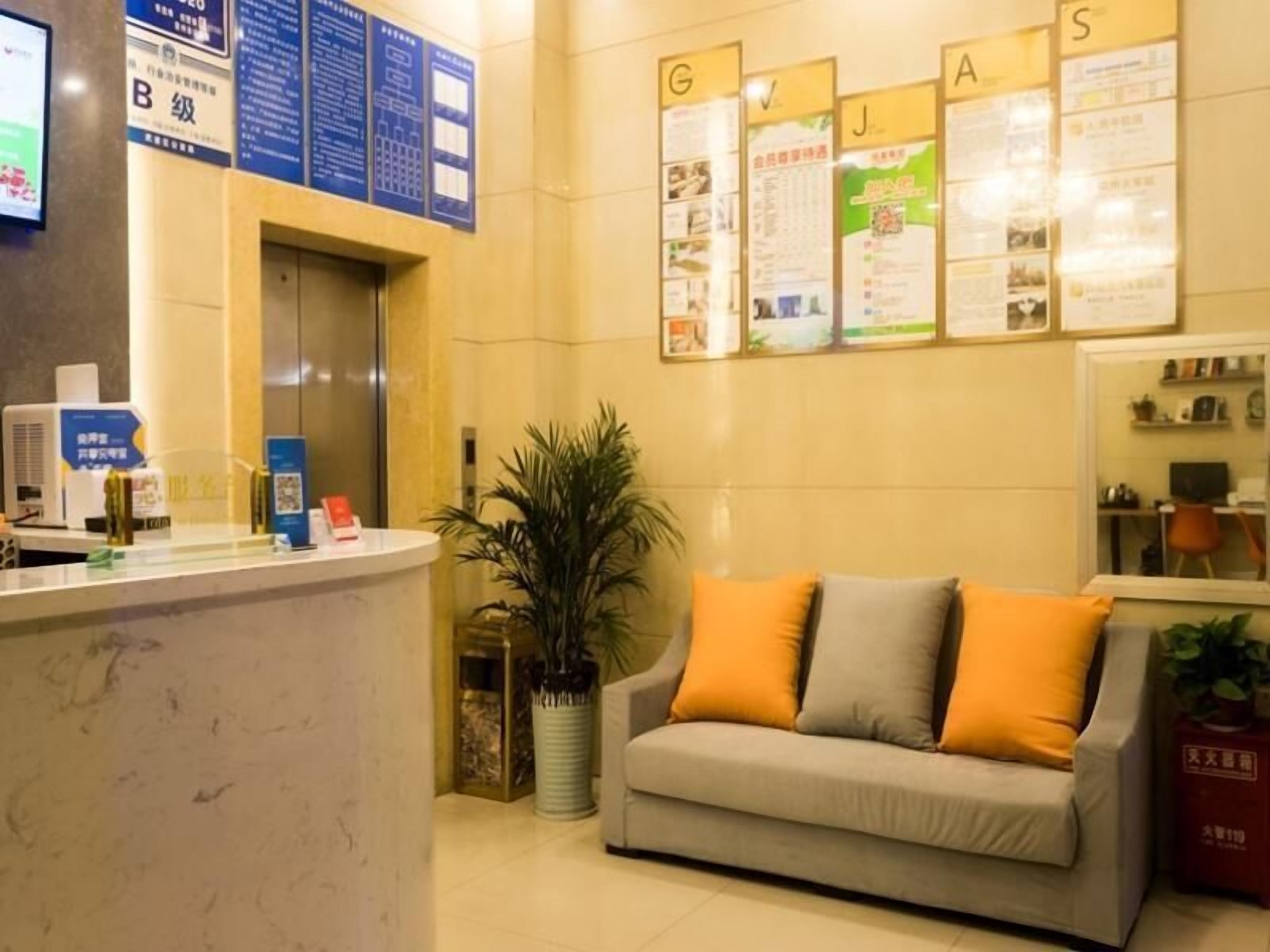 A reception area with a counter, a sofa with orange cushions, a potted plant, and a wall with informational posters.