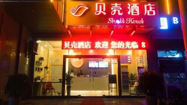 A hotel entrance with a neon sign, reception desk, and a few chairs outside. - Shell Changzhou University City Science and Educat (Changzhou)