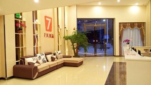 Un vestíbulo de hotel con una recepción, un sofá marrón con cojines, un ventanal grande y una planta.