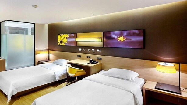 Habitación de hotel con dos camas, un escritorio, una silla, un televisor y un panel de control en la pared.