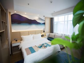 Habitación de hotel con una cama grande, un escritorio, una silla, una mesita de noche, un cuadro en la pared y una ventana con cortinas.