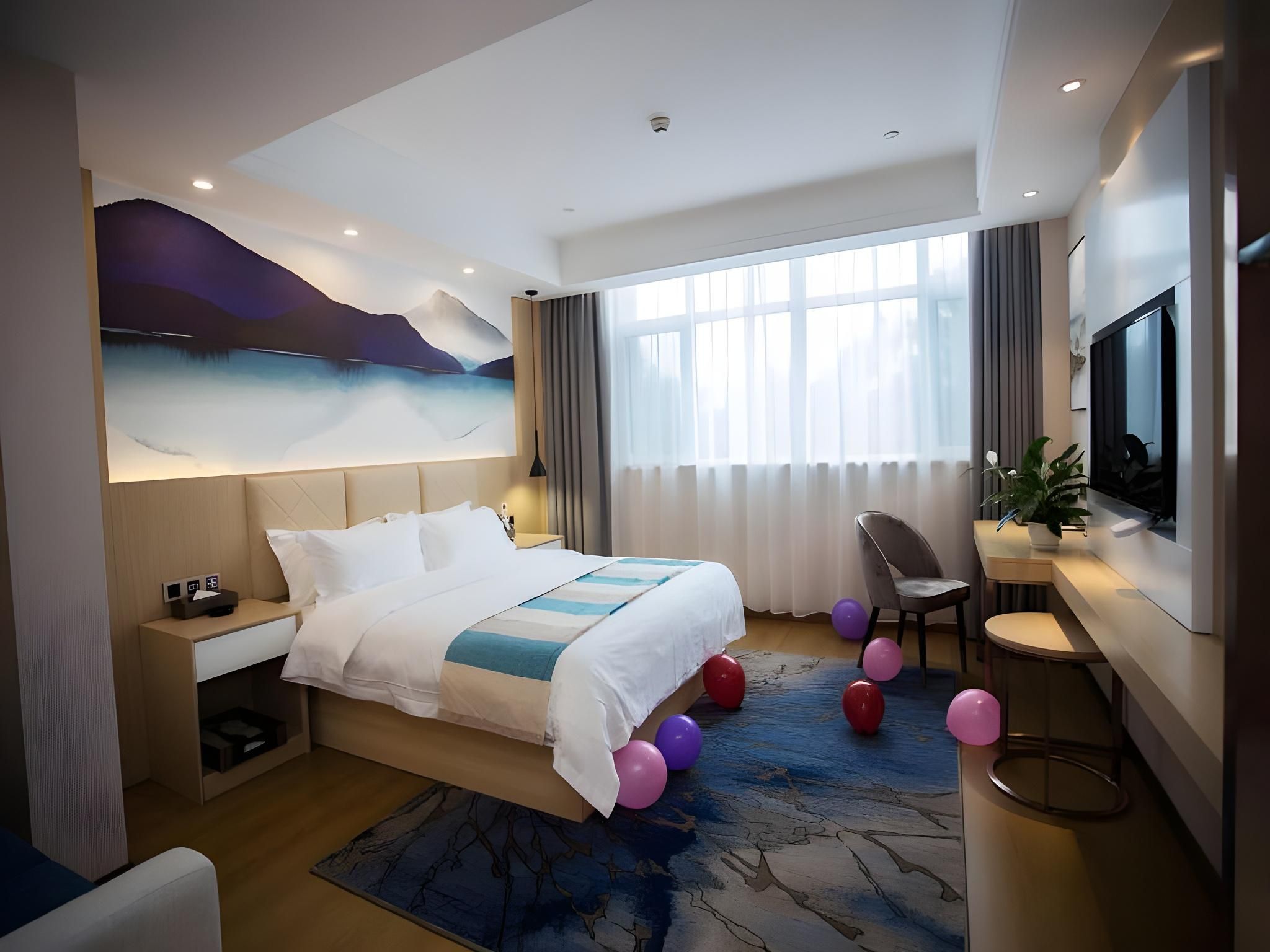 A modern hotel room with a large bed, a desk, a chair, a television, and a large window with curtains.