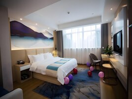 Una habitación de hotel moderna con una cama grande, un escritorio, una silla, un televisor y un amplio ventanal con cortinas.