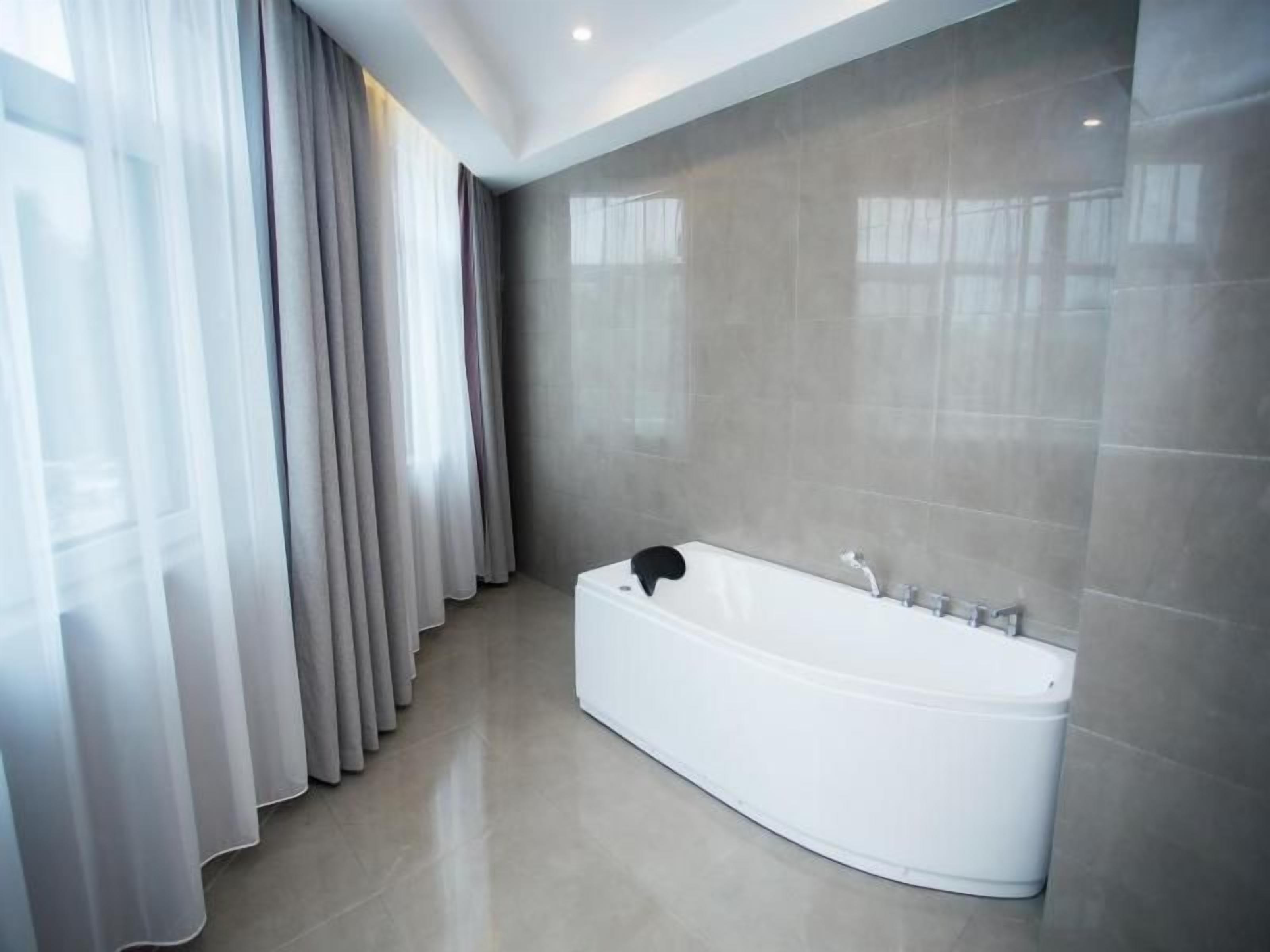 Un baño moderno con una bañera independiente, un espejo grande y una ventana con cortinas translúcidas.