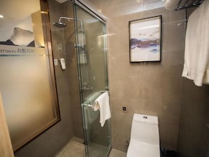 A bathroom with a glass-enclosed shower, a toilet, and a framed picture on the wall.
