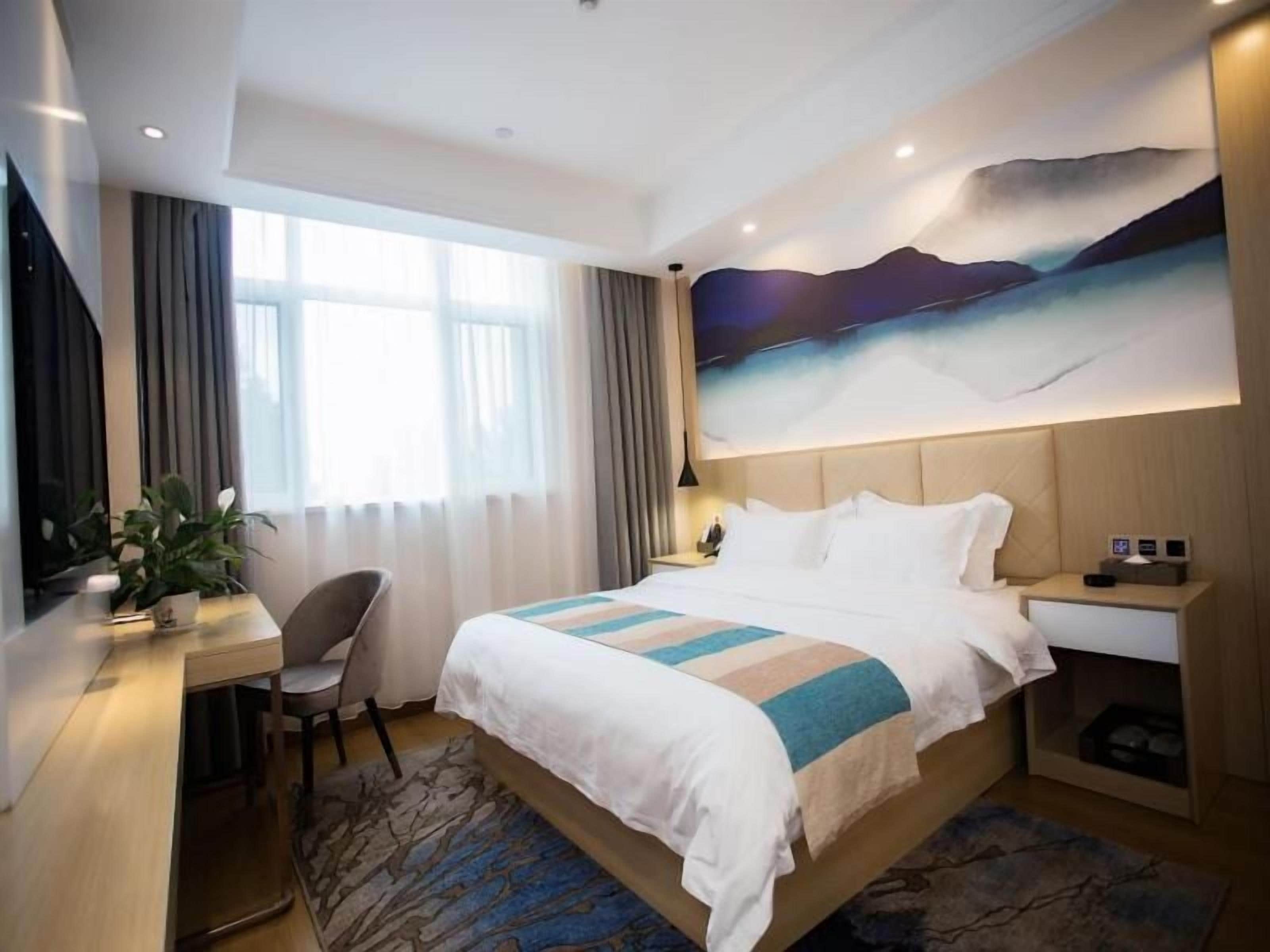 A hotel room with a bed, desk, chair, and a large painting on the wall.