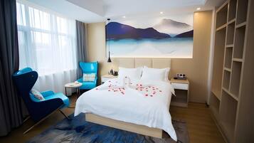A hotel room with a bed, a blue armchair, a nightstand, a large painting of a landscape, and a wooden wardrobe.