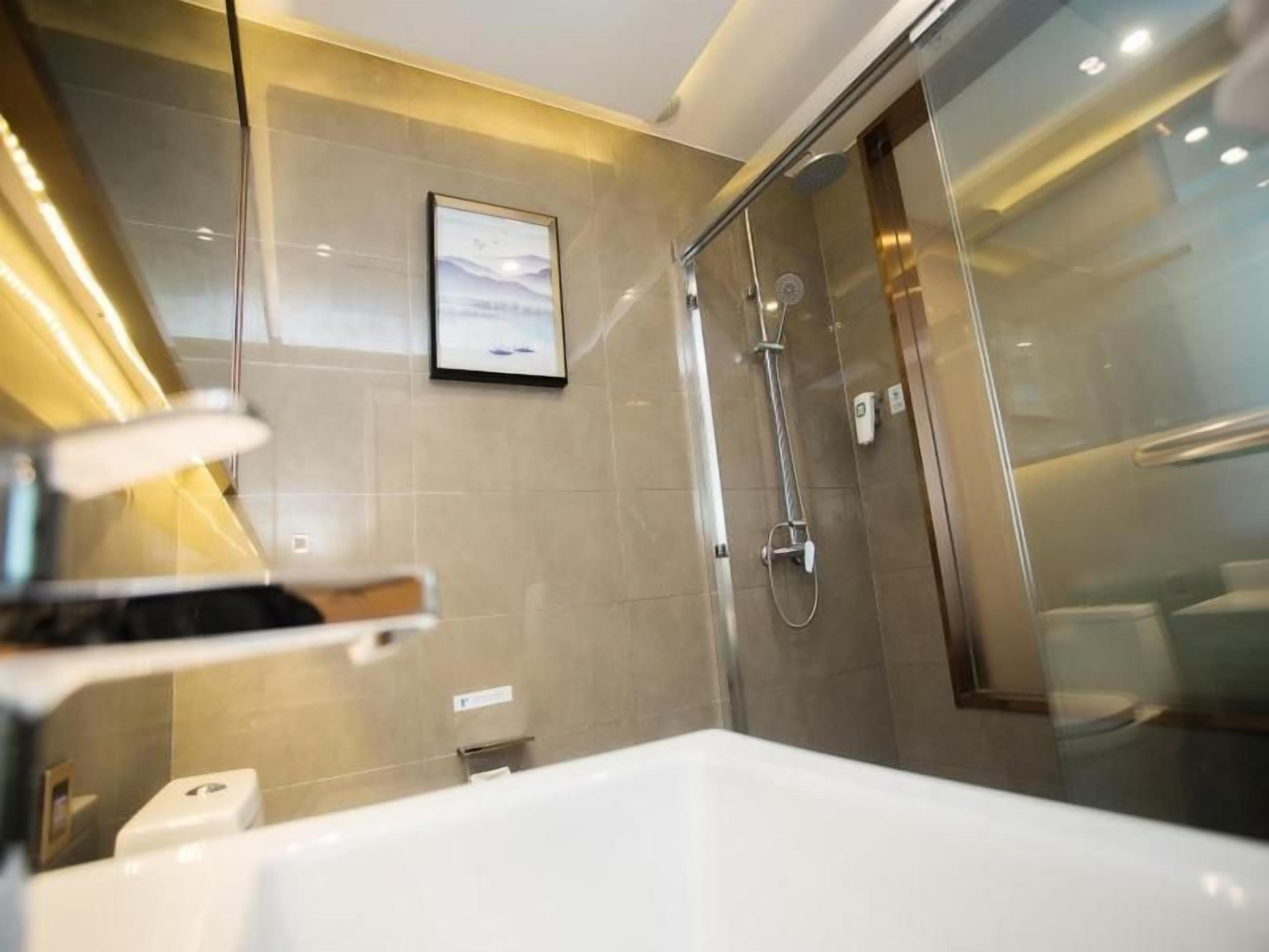 A modern bathroom with a glass shower enclosure, a white bathtub, and a framed picture on the wall.