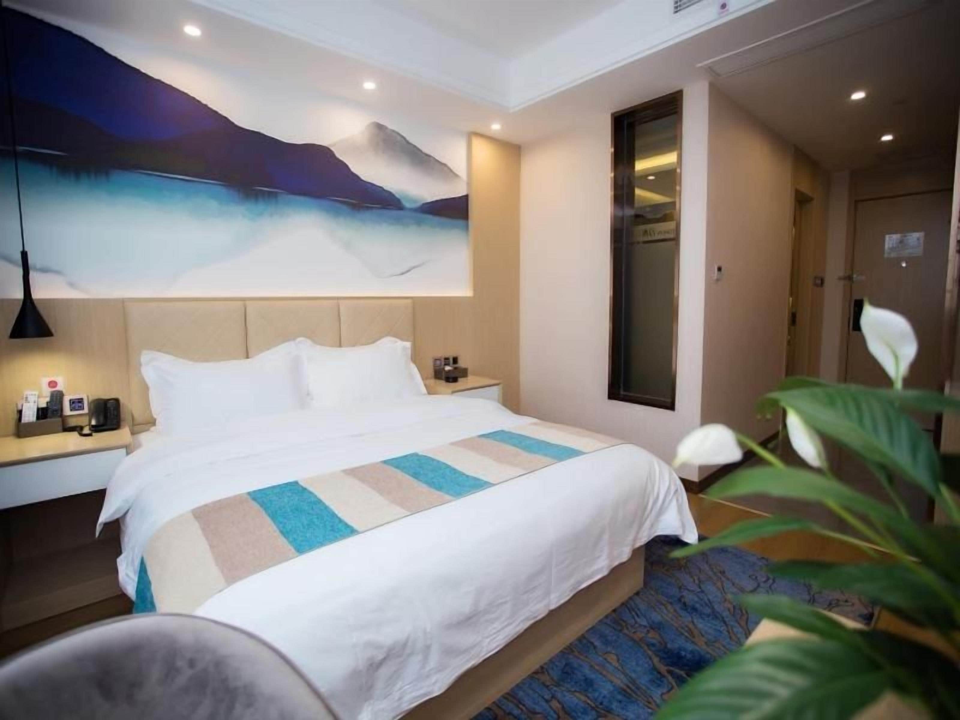 A hotel room with a large bed, a nightstand, a lamp, and a painting on the wall.