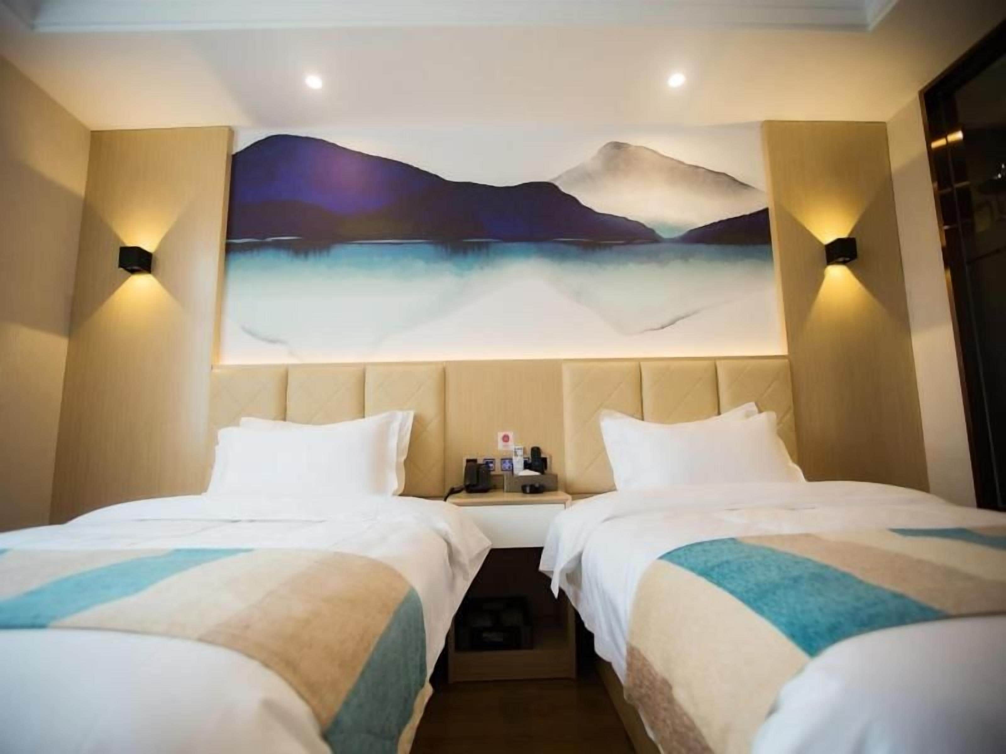 A hotel room with two beds, a painting on the wall, and a nightstand with a lamp.