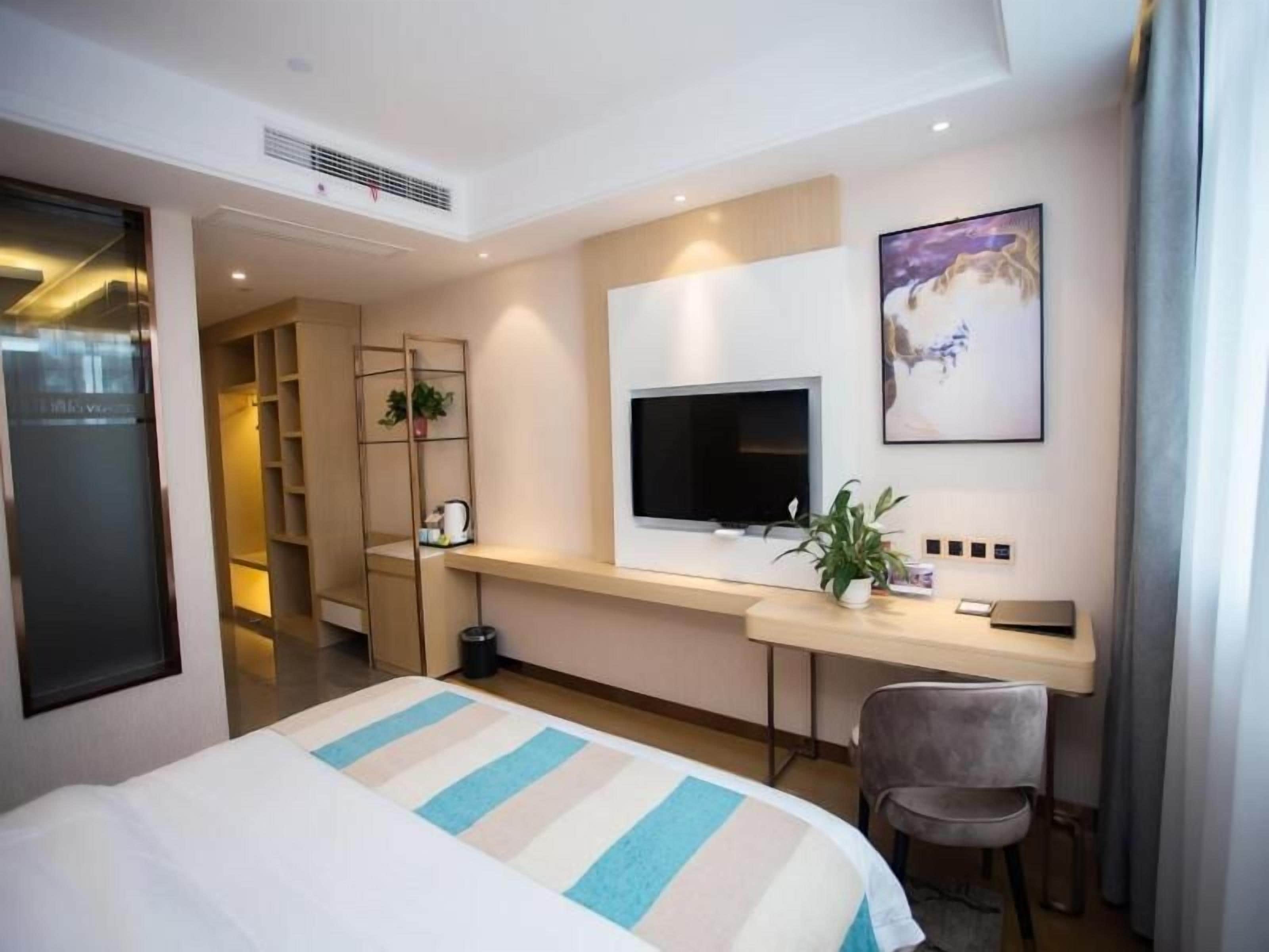 Una habitación de hotel con una cama, un escritorio, un televisor y una planta.