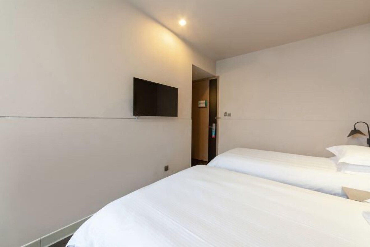 A hotel room with two beds, a flat-screen TV mounted on the wall, and a door leading to another room.