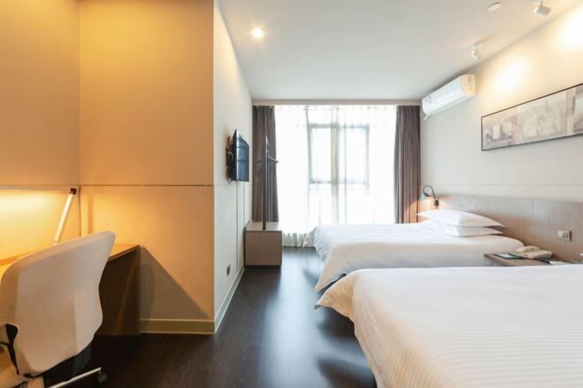 A hotel room with two beds, a desk, a chair, a TV, and a window with curtains.