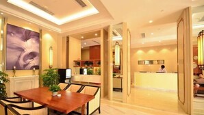 A hotel lobby with a reception desk, a dining area with a wooden table and chairs, and a large abstract painting on the wall. - Jinjiang Inn Select (Wuhan International Expo Center Maying Road Metro Station) (Wuhan)