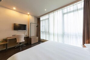 A hotel room with a large bed, a desk with a chair, a TV mounted on the wall, and a window with curtains. - Jinjiang Inn Select (Wuhan International Expo Center Maying Road Metro Station) (Wuhan)