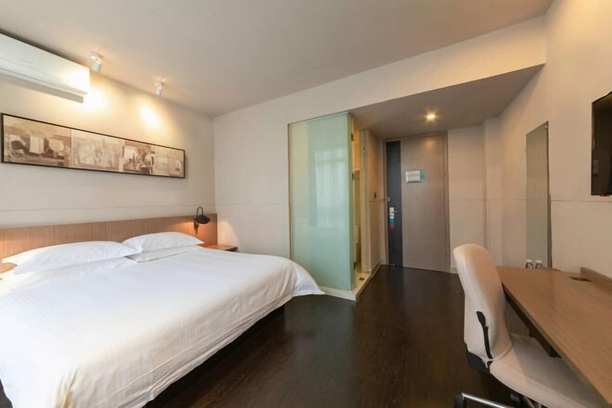 A hotel room with a bed, bedside table, lamp, and a desk with a chair.
