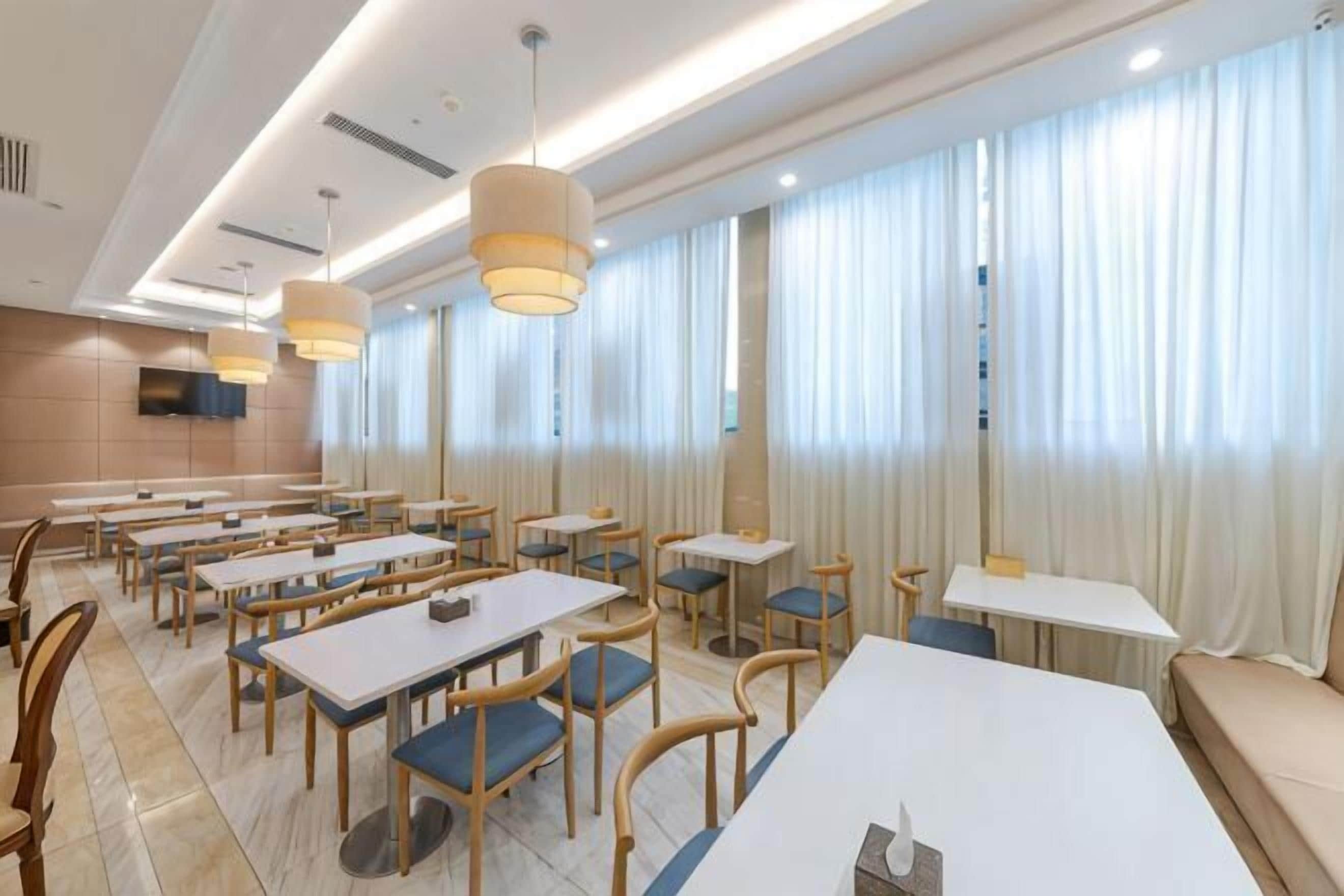 A restaurant with multiple tables and chairs, a television mounted on the wall, and large windows with curtains.