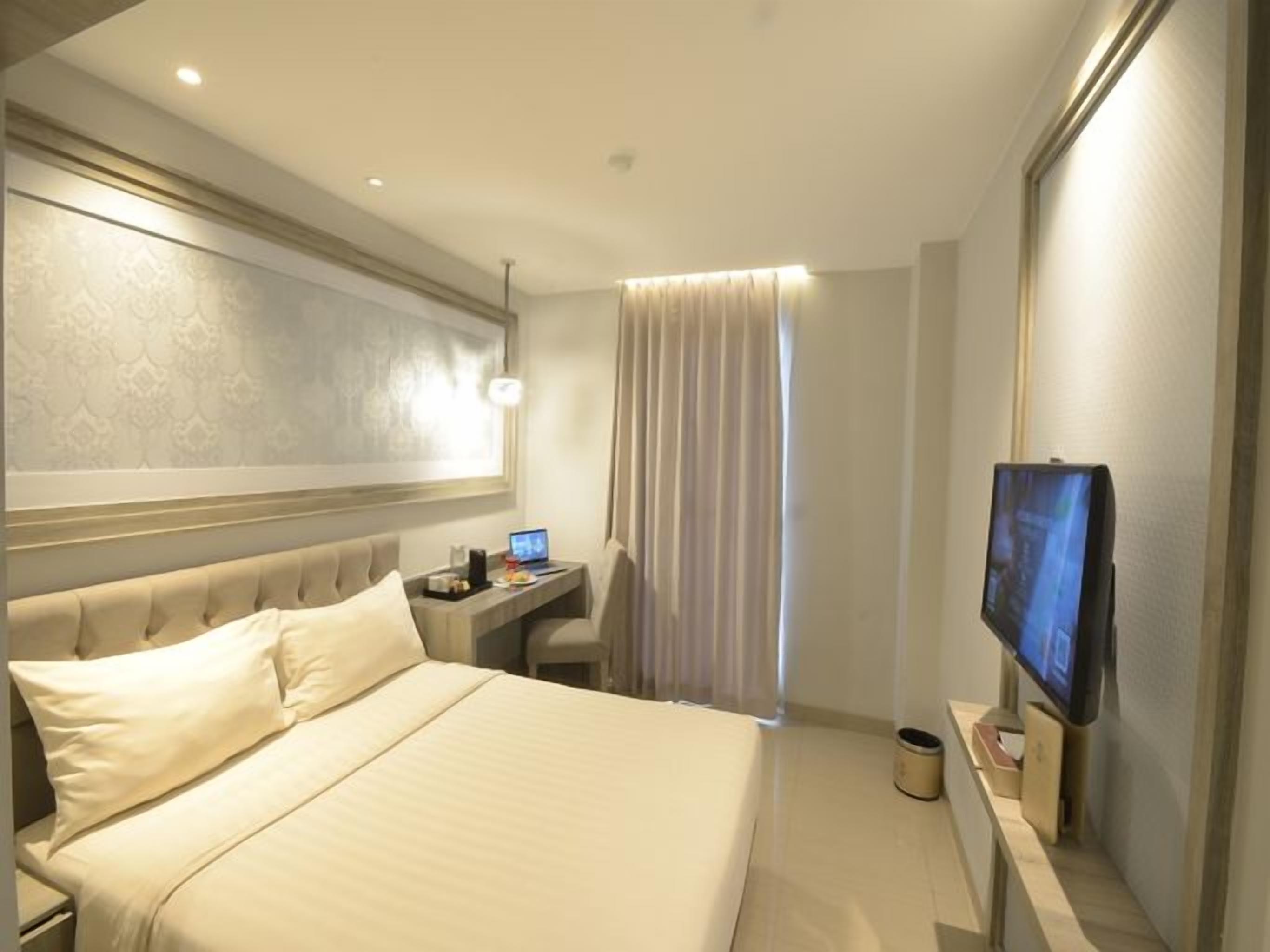 A hotel room with a large bed, a desk with a computer, a television, and a window with curtains.