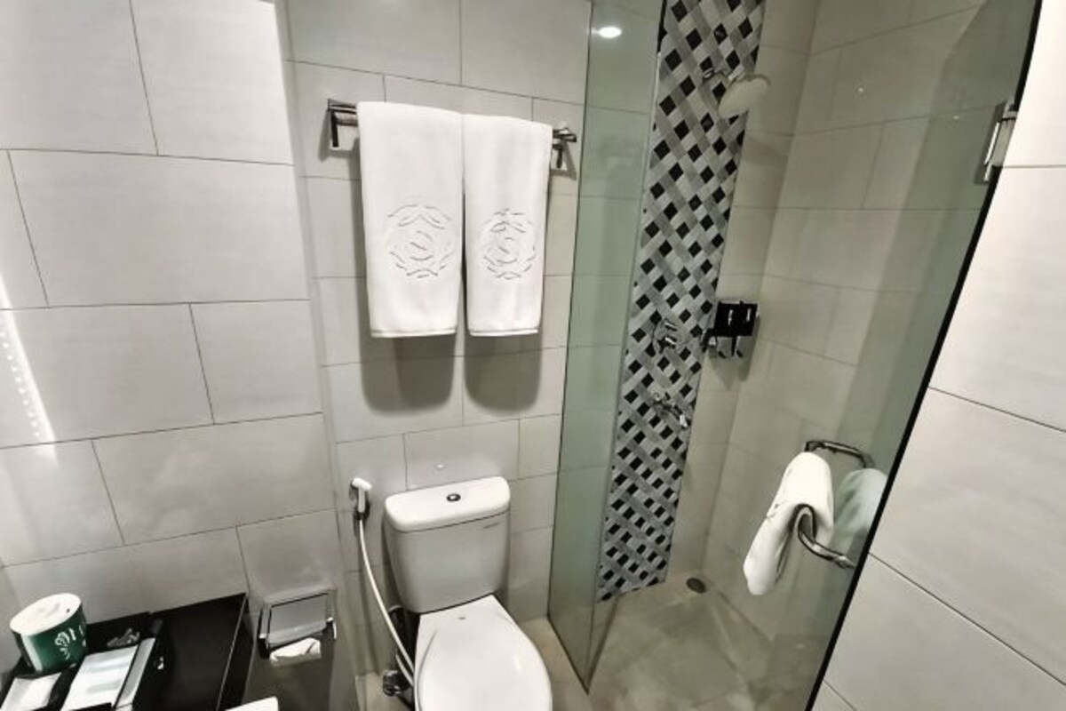 A bathroom with a toilet, a glass shower enclosure, and a towel rack with two towels.