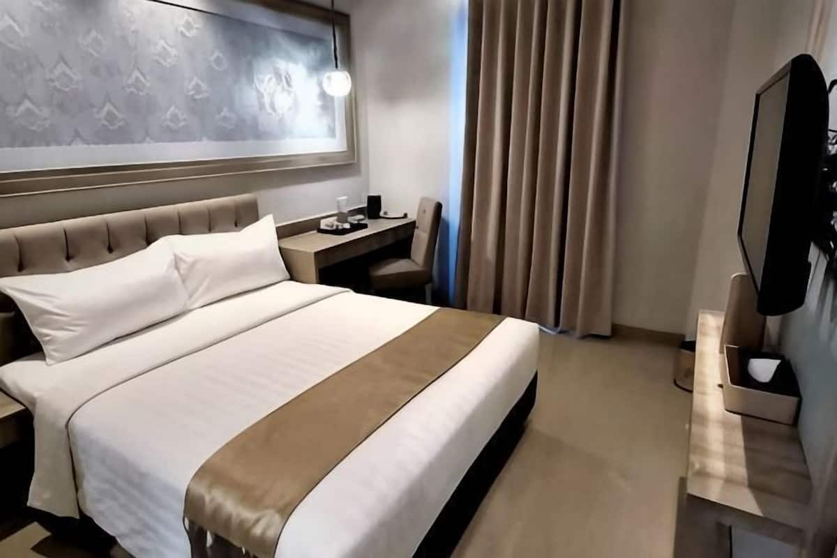 Ett hotellrum med en stor säng, ett skrivbord, en stol, en tv och ett fönster med gardiner.