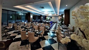 Un restaurant spacieux avec un sol à carreaux, de nombreuses tables et chaises, et un bar situé au fond de la salle.
