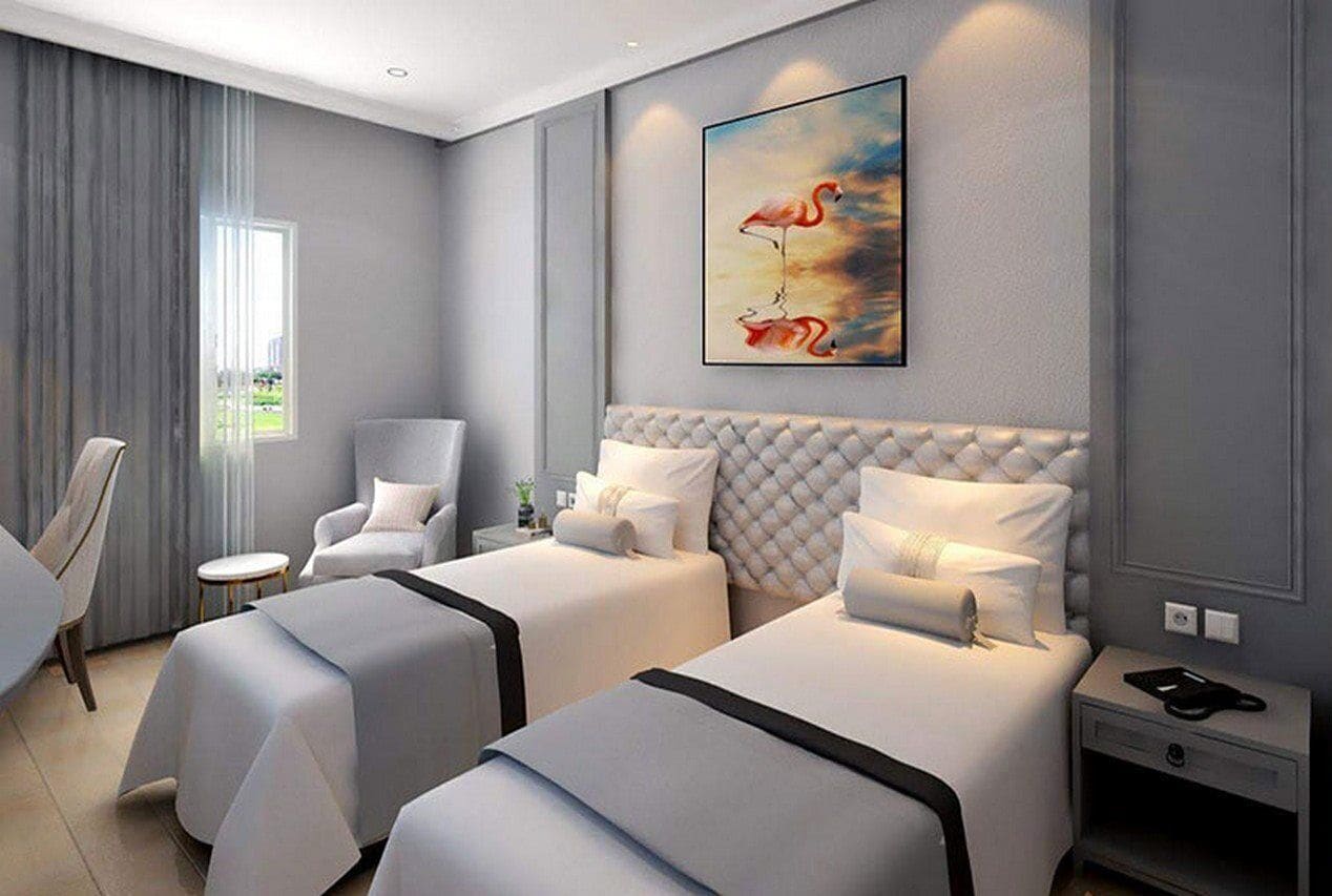 A hotel room with two beds, a chair, a small table, and a painting on the wall.
