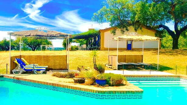 A pool area with lounge chairs, a covered seating area, and a building with a thatched roof. - Monte Alentejano T5 Private Pool (Portalegre)