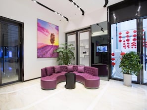 A modern lobby with a curved purple sofa, a large painting of a sunset, and a glass wall with red lanterns. - Lavande Hotels (Chengdu)