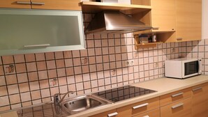 Een keuken met een RVS-gootsteen, een magnetron en houten keukenkastjes.