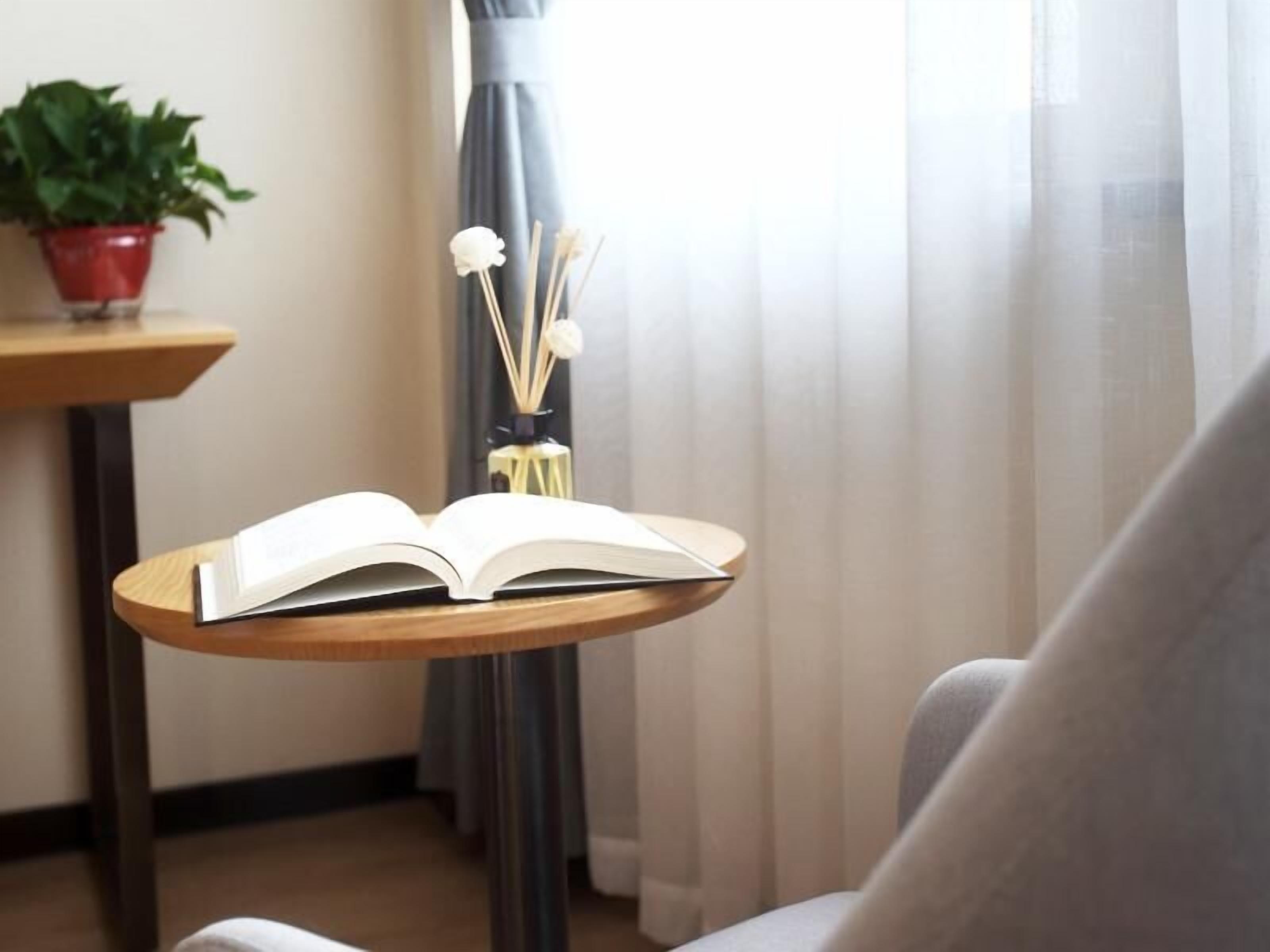 Um livro aberto sobre um suporte de madeira em um quarto com uma planta e um vaso com raminhos.