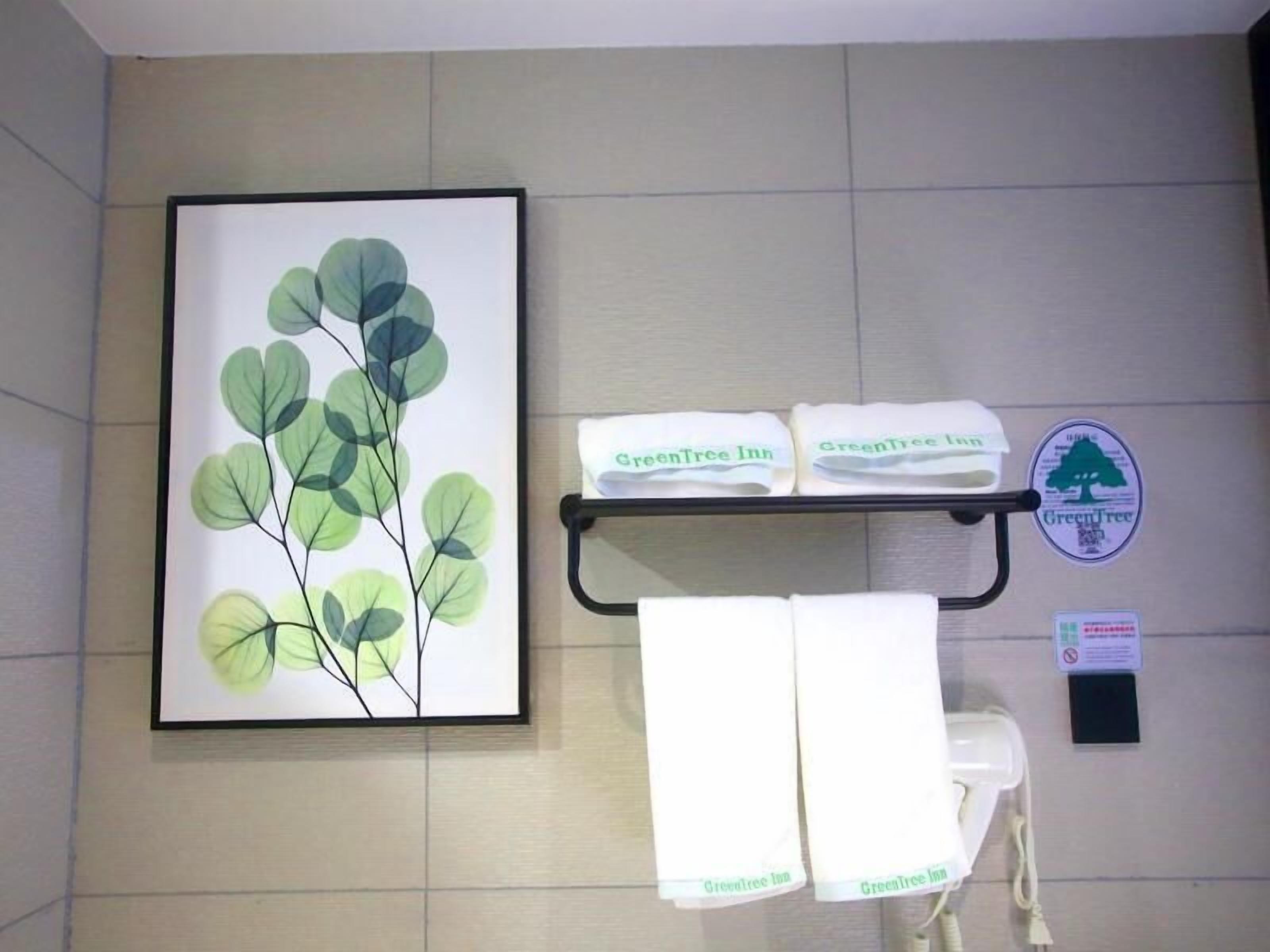 A bathroom with a framed botanical print, a towel rack with GreenTree Inn towels, and a GreenTree Inn logo.