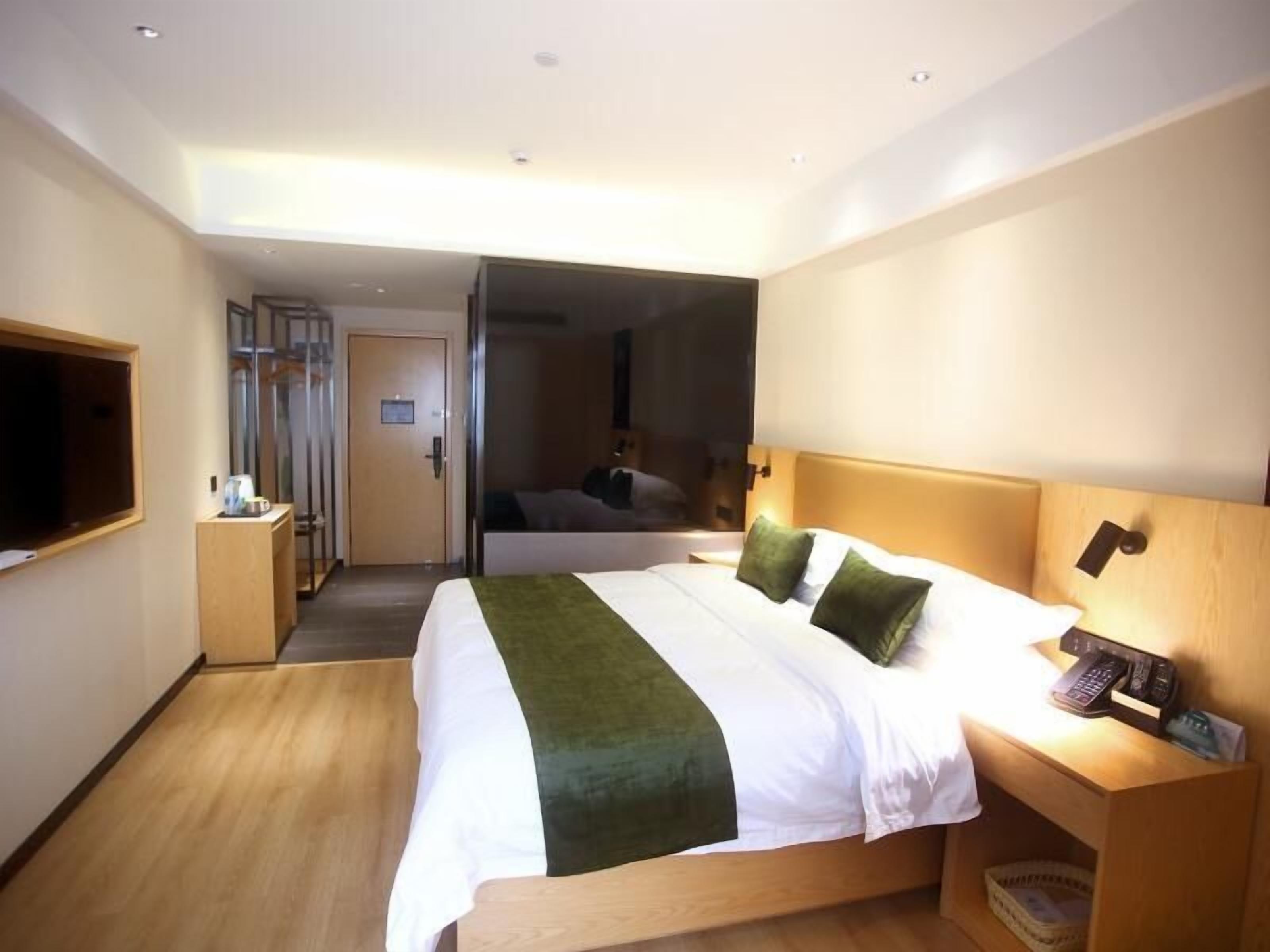 A modern hotel room with a large bed, a wooden nightstand, a TV, and a door leading to another room.