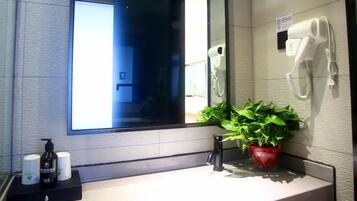 A bathroom with a large mirror, a sink, a hairdryer, and a potted plant.