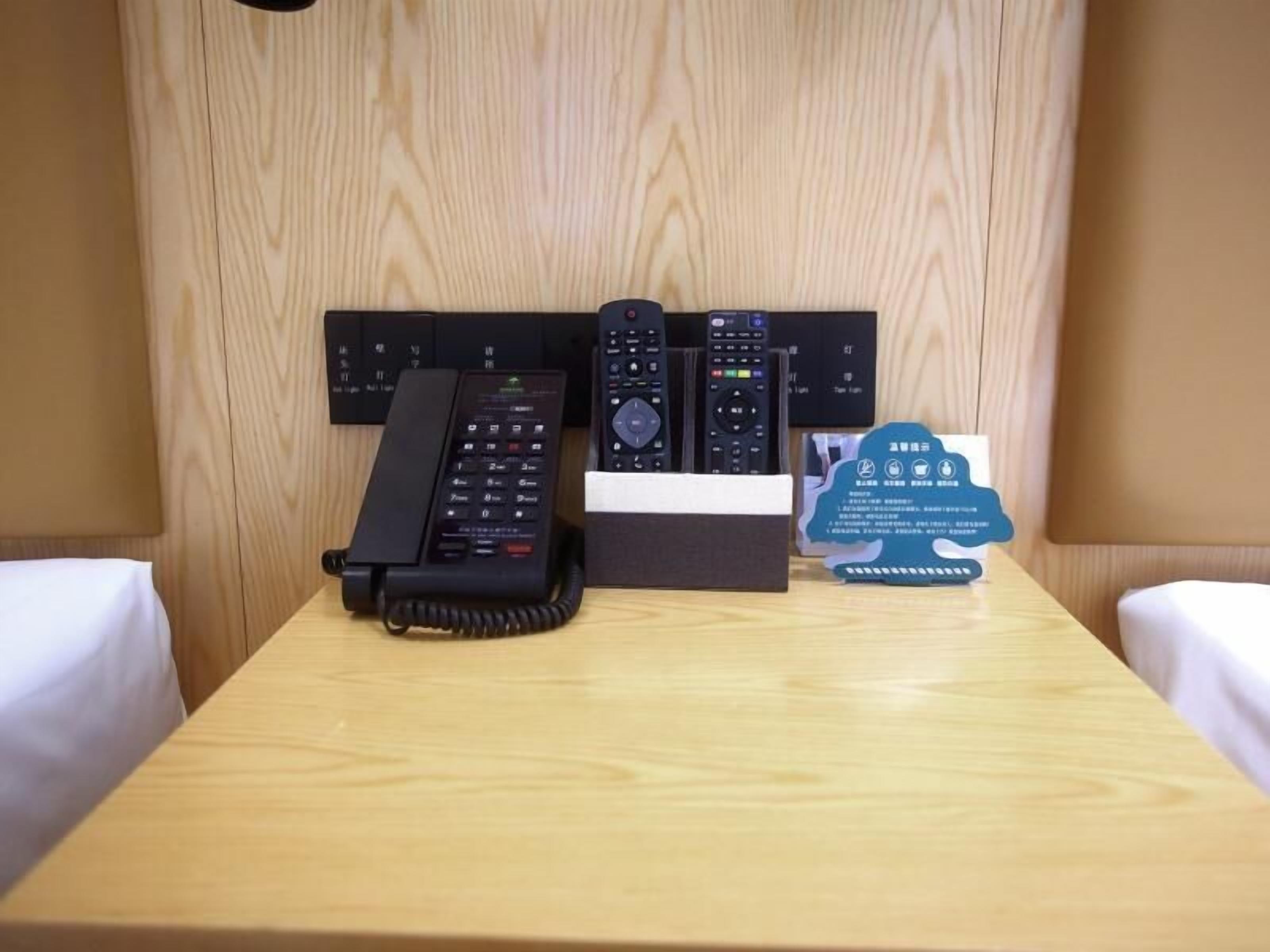 Une chambre d’hôtel avec une tête de lit en bois, un téléphone, une télécommande et un panneau d’affichage contenant des informations sur l’hôtel.
