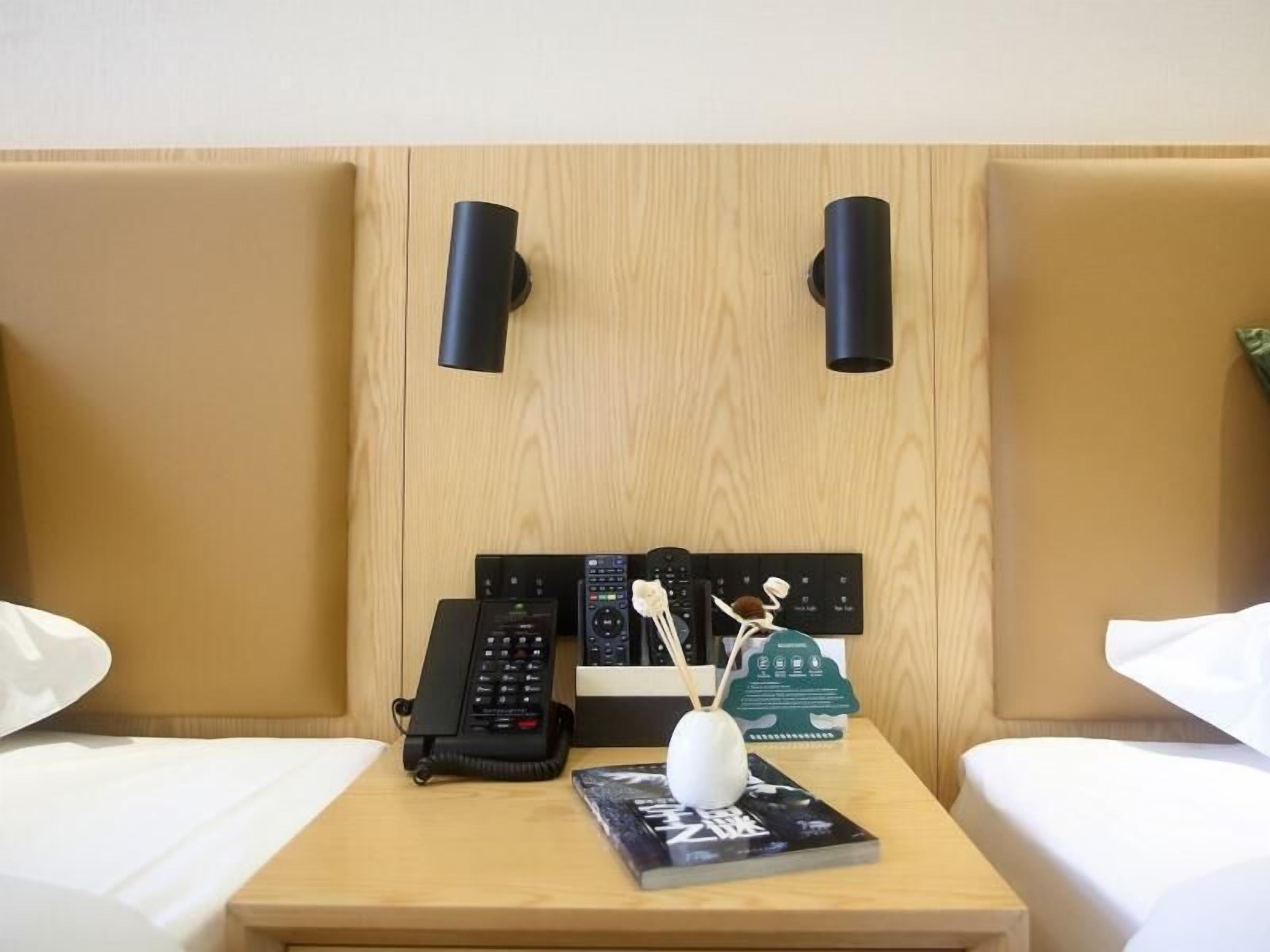 Et hotelværelse med to senge, et sengebord med telefon, fjernbetjening, en dekorativ genstand og en bog.