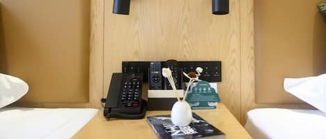 A hotel room with two beds, a bedside table with a phone, a remote control, a decorative item, and a book.