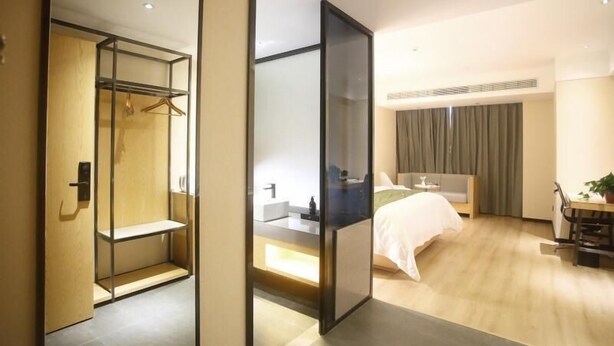 A modern hotel room with a walk-in closet, a bed with a green bedspread, a bedside table, and a large window with curtains. - Greentree Inn Fuyang Exhibition Center (Fuyang)
