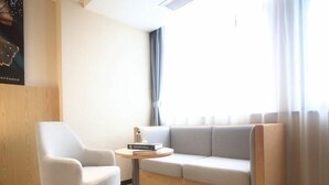 A modern room with a white sofa, a white armchair, and a small round table with a lamp. - Greentree Inn Fuyang Exhibition Center (Fuyang)